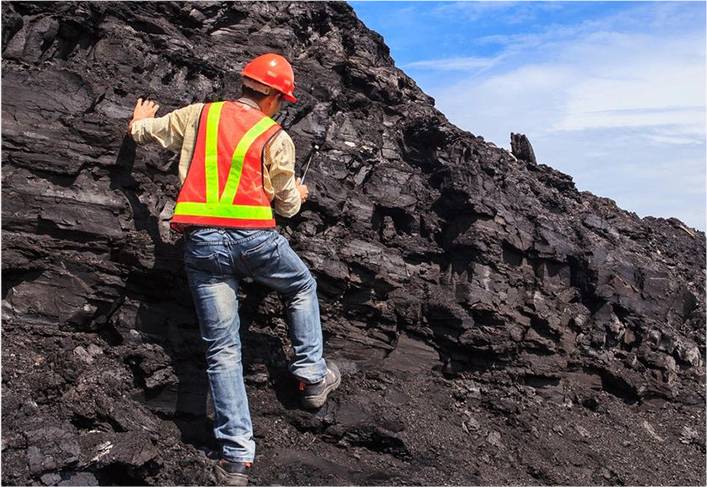 A man in an orange vest climbing up a pile of coal.