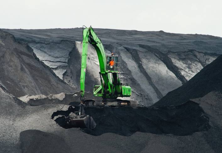 A green crane is in the middle of an open pit.